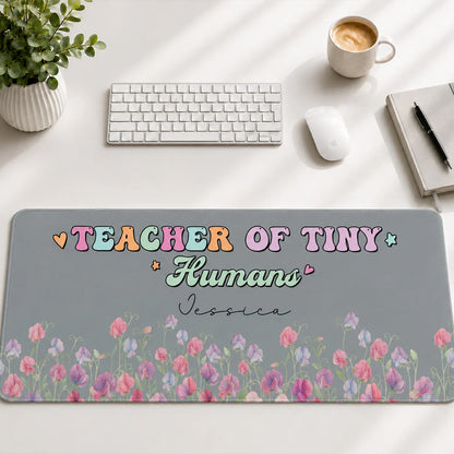 Personalized teacher desk mat with 'Teacher of Tiny Humans' text and colorful floral design on a gray workspace background