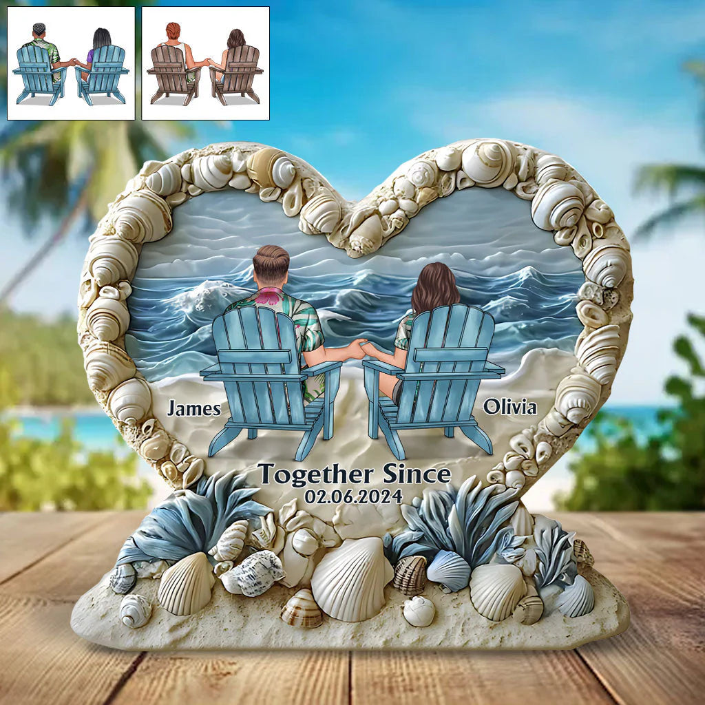 Personalized anniversary plaque shaped like a heart with seashells and a couple sitting on beach chairs looking at the ocean.